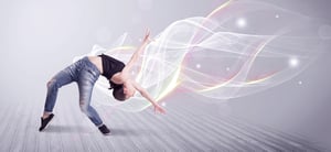 A beautiful young hip hop dancer dancing contemporary urban street dance in front of grey wall background with smokey lines and glitter concept.