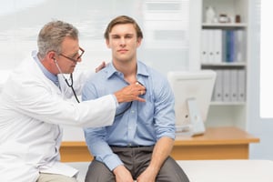 Mature doctor listening to his patients chest with stethoscope in his office at the hospital