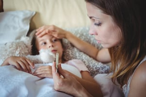 Mother checking daughters temperature on thermometer at home