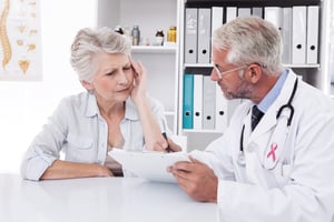 Pink awareness ribbon against female senior patient visiting a doctor